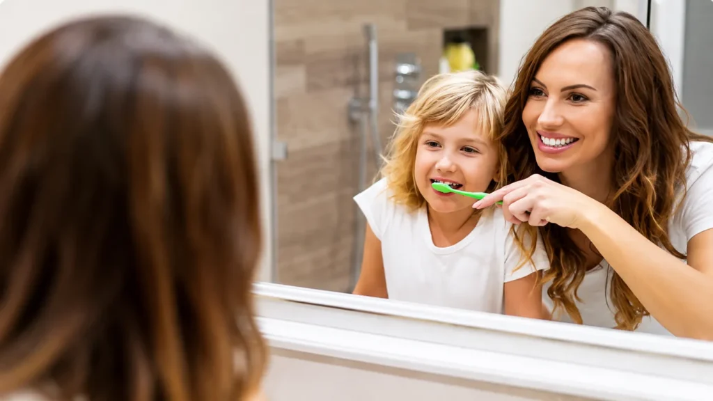 Mamma che insegna alla figlia la tecnica corretta di spazzolamento dei denti davanti allo specchio per prevenire il tartaro